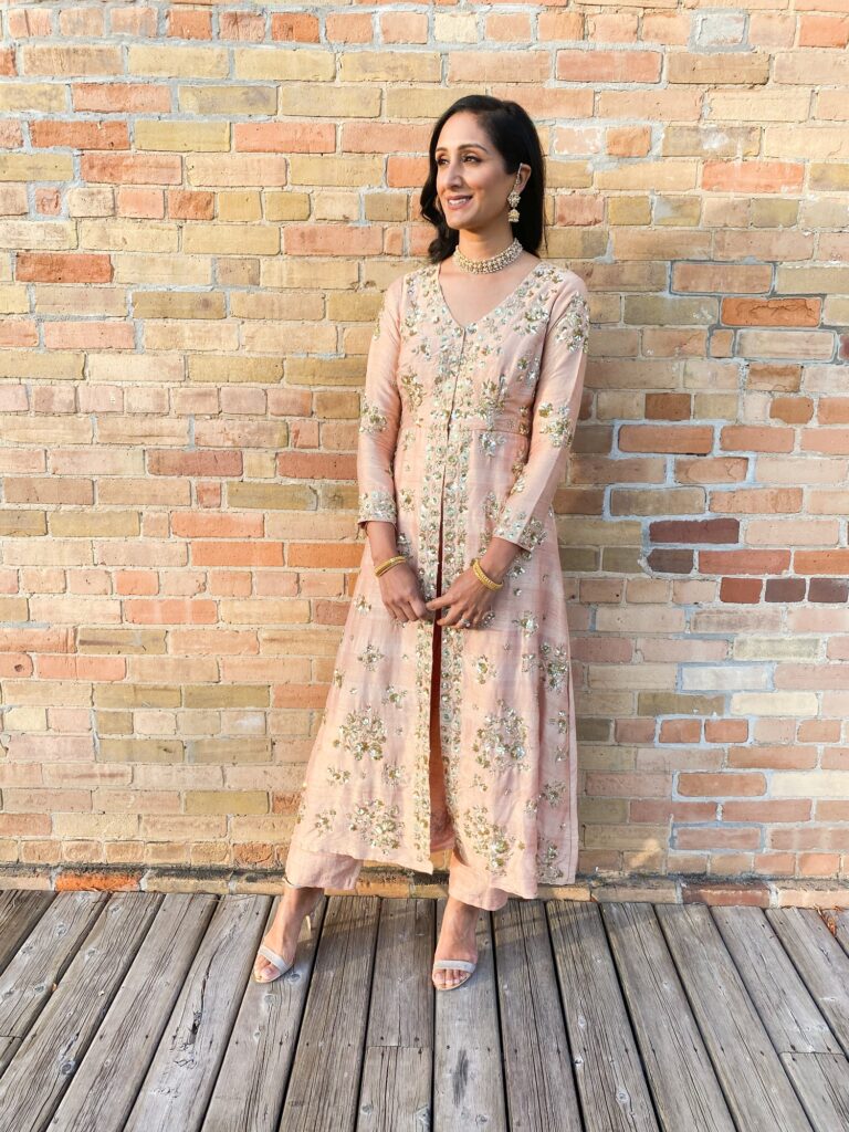 Standing against a brick wall in an Astha Narang outfit